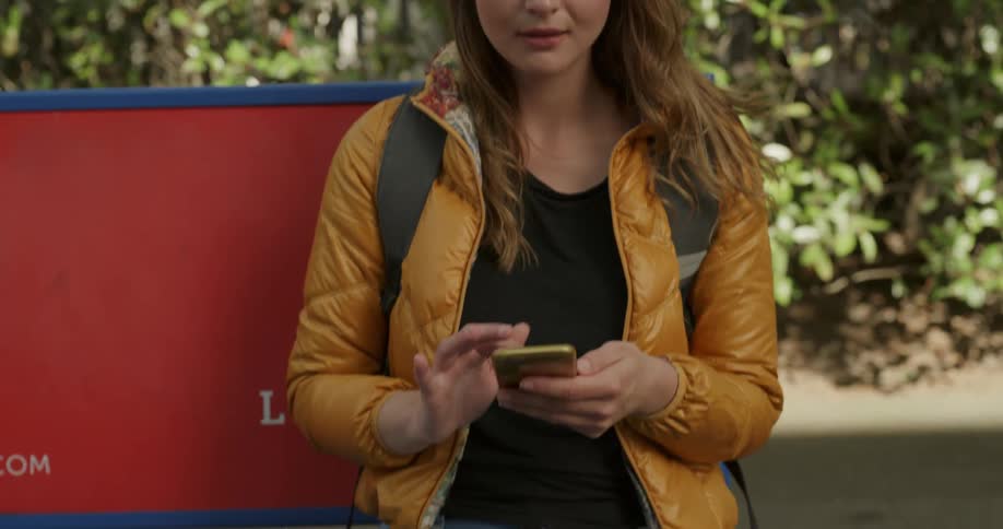 A young woman uses her smartphone while sitting outdoors on a bench during the day