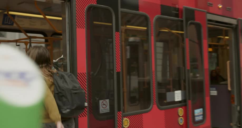 A woman wearing a backpack boards a commuter train