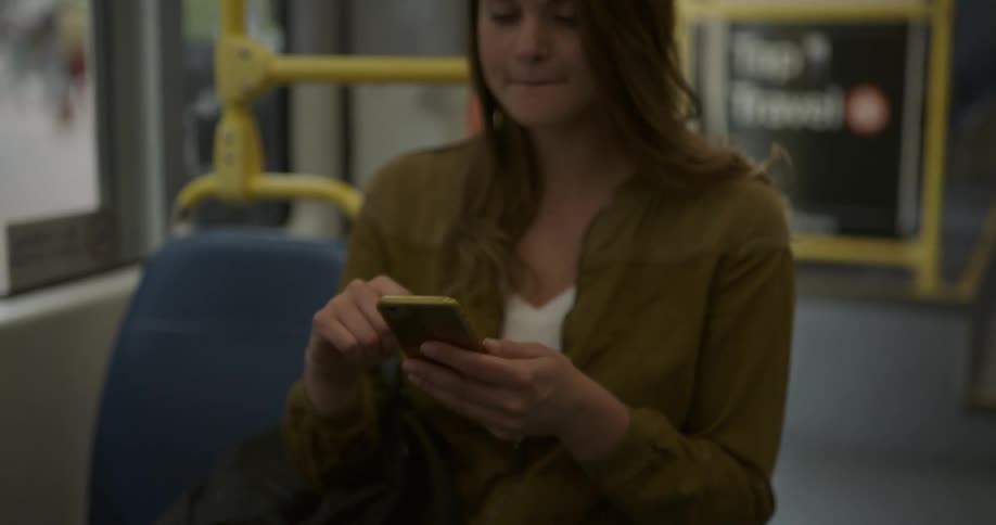 A woman sits on a public bus swiping through her cell phone