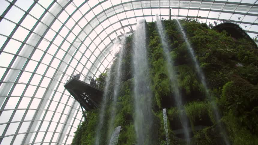 Large indoor exhibit covered in grass and shrubbery with small waterfalls cascading from the top and middle sections