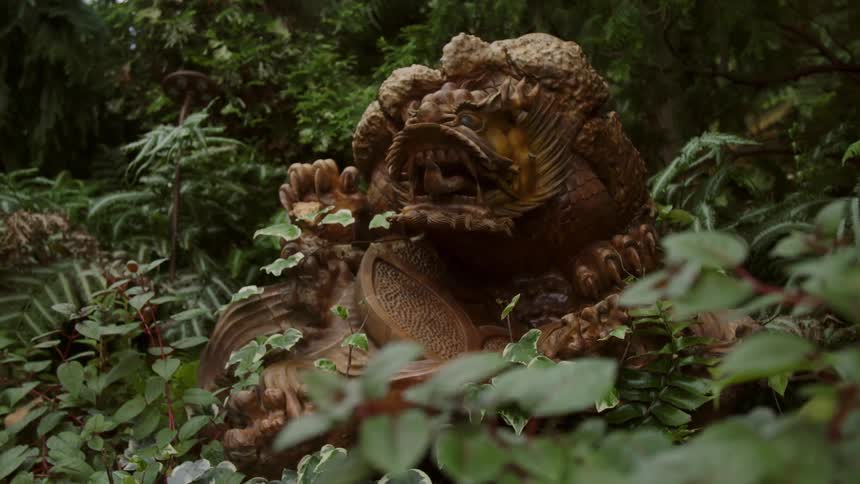 A statue of a dragon like creature sits in a lush garden