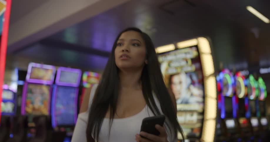 A woman is walking through a casino while looking at her smartphone