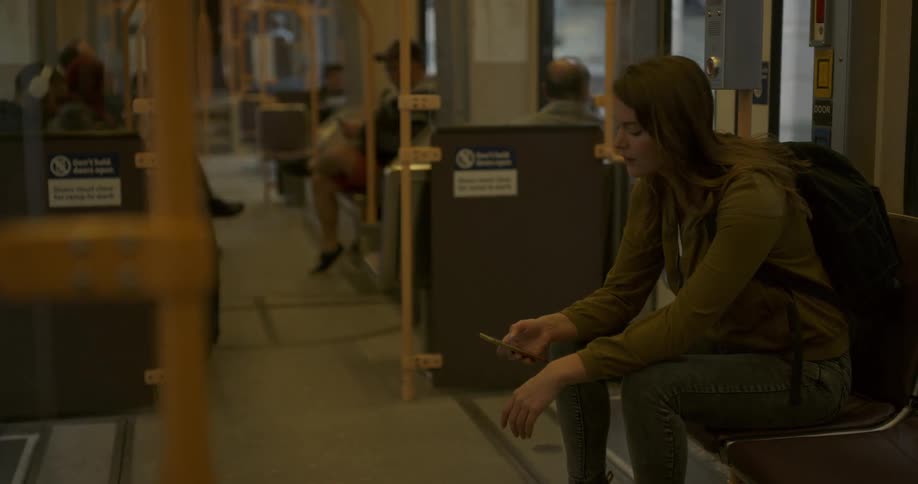 A young woman sits on a train looking out the window and testing on her phone