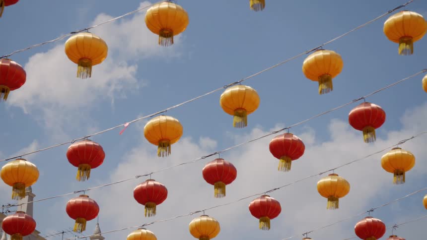 Red and yellow lanterns hang from a line beneath a blue daytime sky