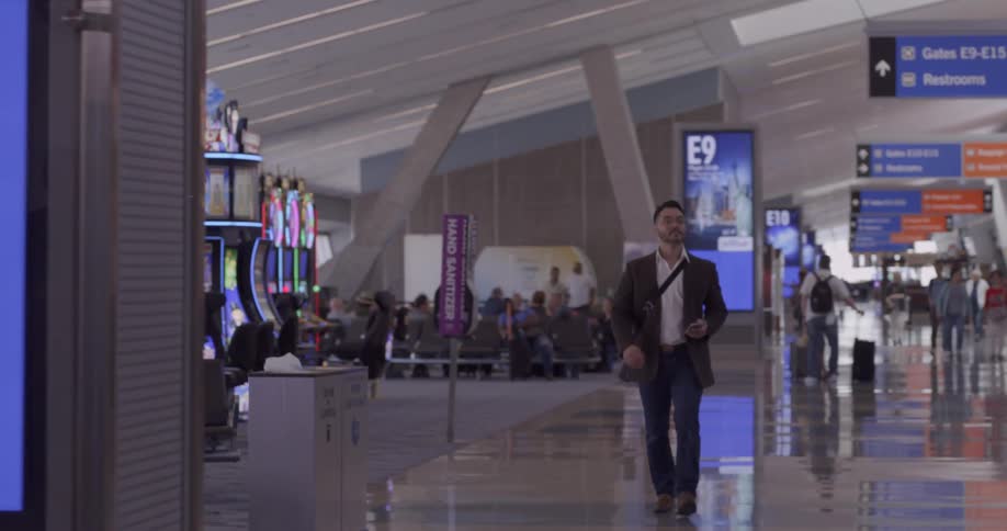 A man walks through an airport terminal holding a cell phone