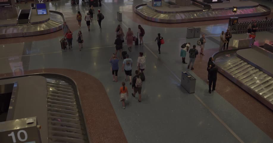 An elevated view of an airport interior with travelers walking and waiting for their luggage