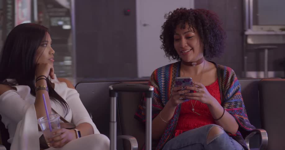 Two women sit talking while they wait near their luggage