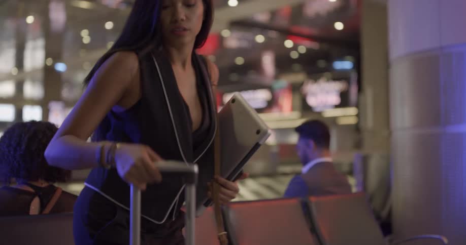 A young woman pulls luggage along behind her as she takes a seat in the waiting area of an airport