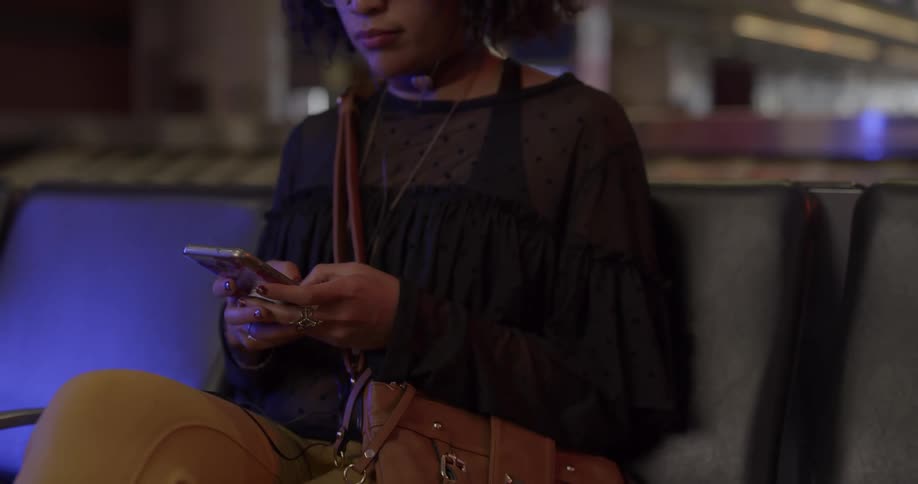 A woman sits in an airport and scrolls through her cell phone