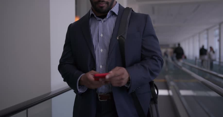 A man checks his phone while standing on an automatic walkway in an airport