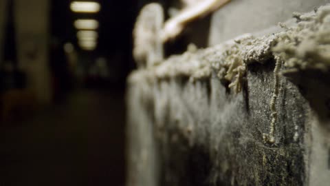 Light blinks at end of corridor in dark warehouse housing old labeled cartons showing stuffing