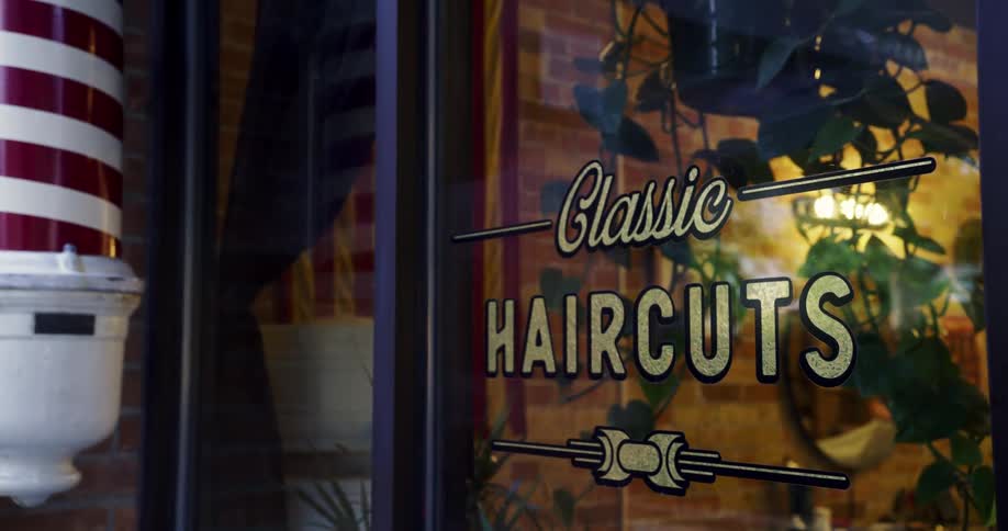 A view inside of a barber shop from the outside at dusk