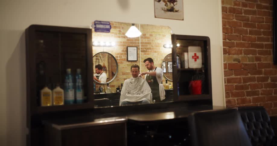 A male barber combs and cuts the hair of a male client