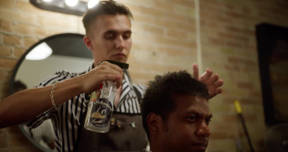 A barber sprays a clients hair with water to prep him for a haircut