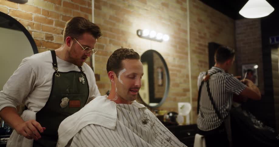 A man gets his neck shaved by a barber in a busy salon