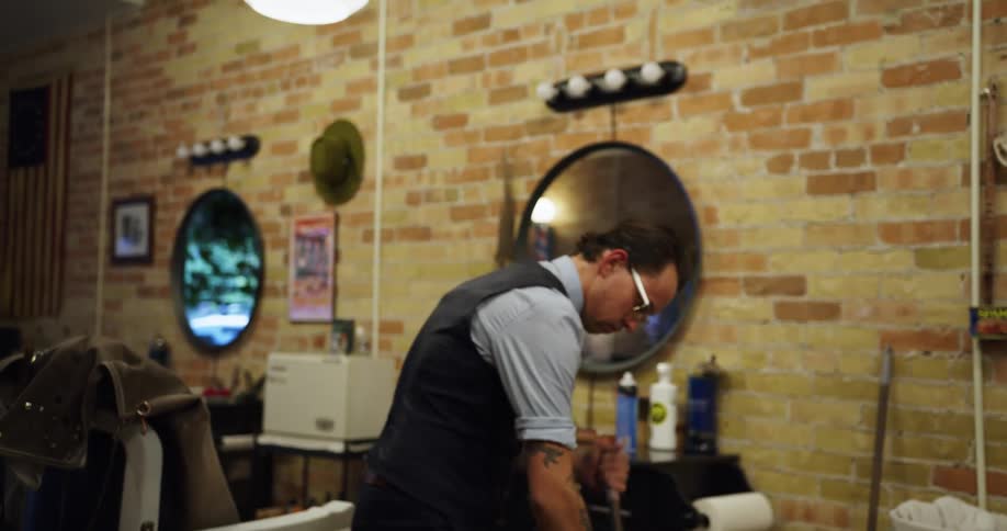 Man sweeps floor in barber shop around barber chair