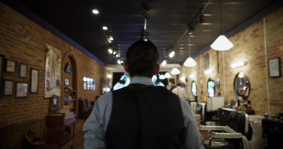 A man walks through a barber shop past people getting haircuts and people waiting