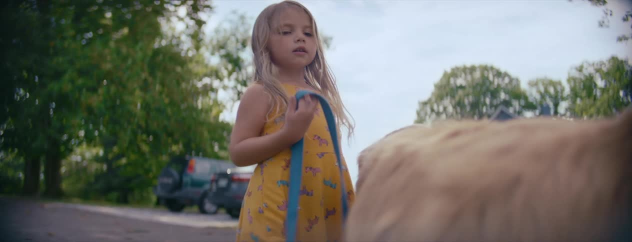 Young blonde girl in a yellow dress pets her golden retriever in front of a house at morning