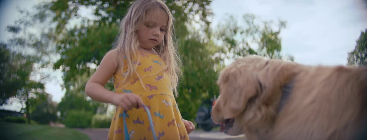 A little girl is playing with her leashed dog in a residential driveway on a cloudy day