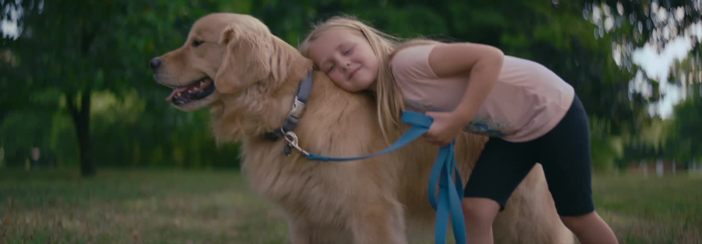 A young girl leans over and hugs her dog tightly standing outside