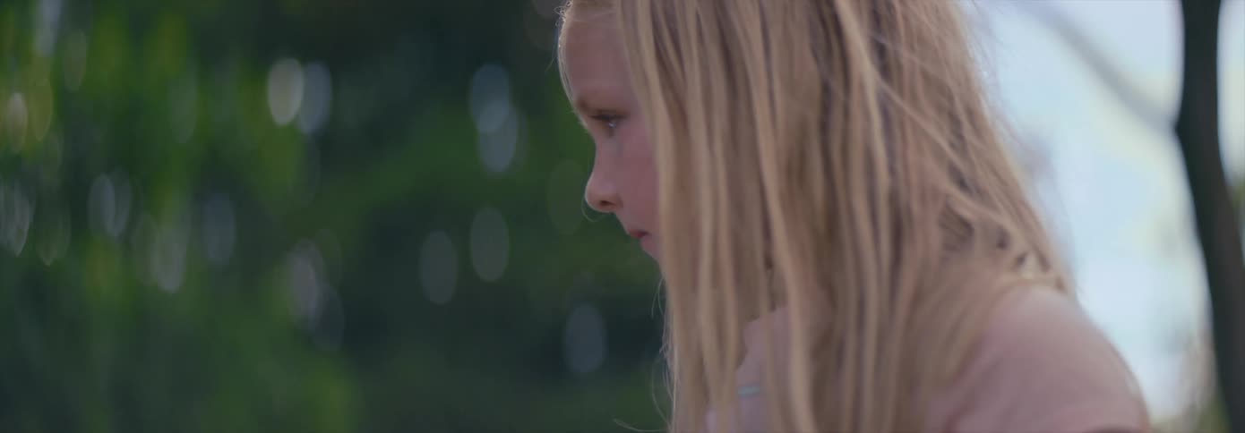 A young blonde haired girl looks at the camera with a slight smile before looking away