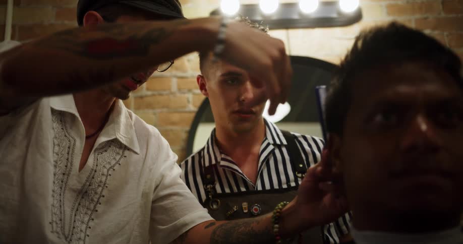 A barber watches closely as another barber cuts a mans hair in a salon