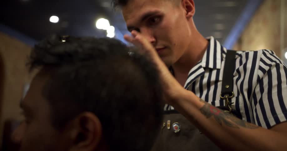 A barber styles the hair of a client in a barber shop during the day