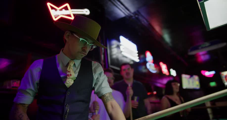 A small group of people are standing around watching a man play in a pool game inside a sports bar
