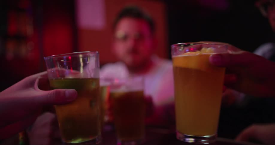 A group of men at a bar clink their drinking glasses together before drinking