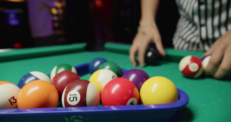 A man sets pool balls up on a pool table in an arcade