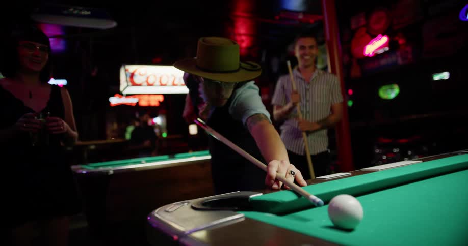 People play pool near signs advertising beer brands