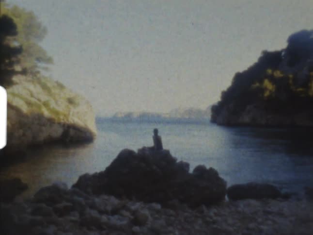 A person sitting on a large rock on a rocky beach in the daytime on 8mm