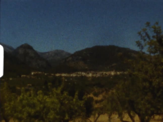 Town is surrounded by vegetation and low mountains under clear blue sky on 8mm