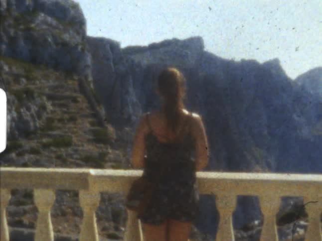 Teen girl stands alone on the balcony looking at the mountains ahead on 8mm