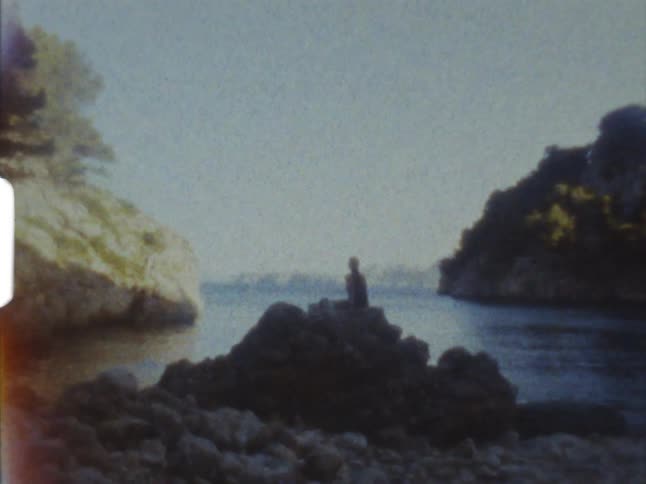 Vintage 8mm film of a person sitting over a rock pile on the coast of a beach
