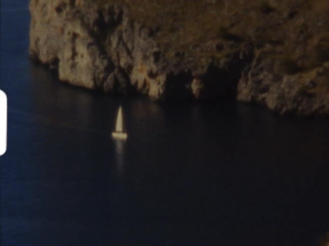 Ocean reflect boat moving across surface of water leaving wake near promontory on 8mm