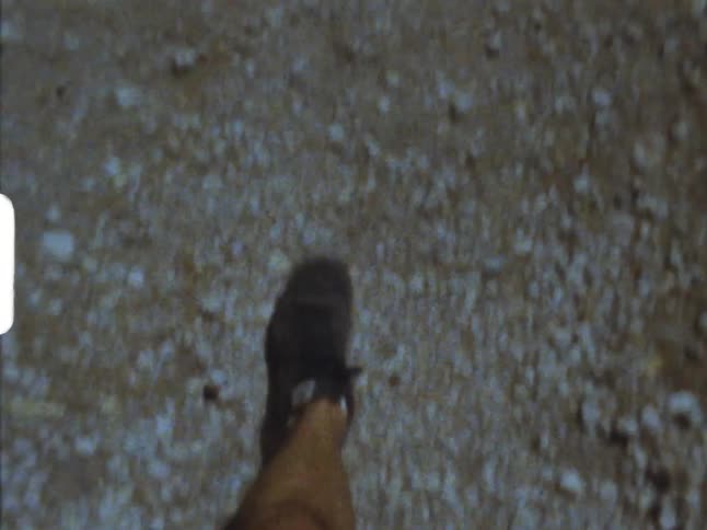 Man wearing shorts walks across pebble strewn ground on 8mm