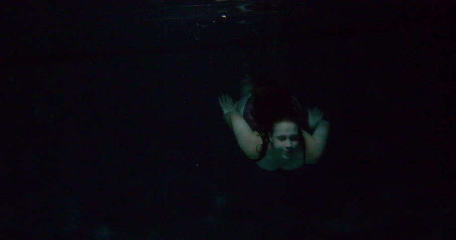 Woman swims through dark underwater wearing swimsuit before rising to surface