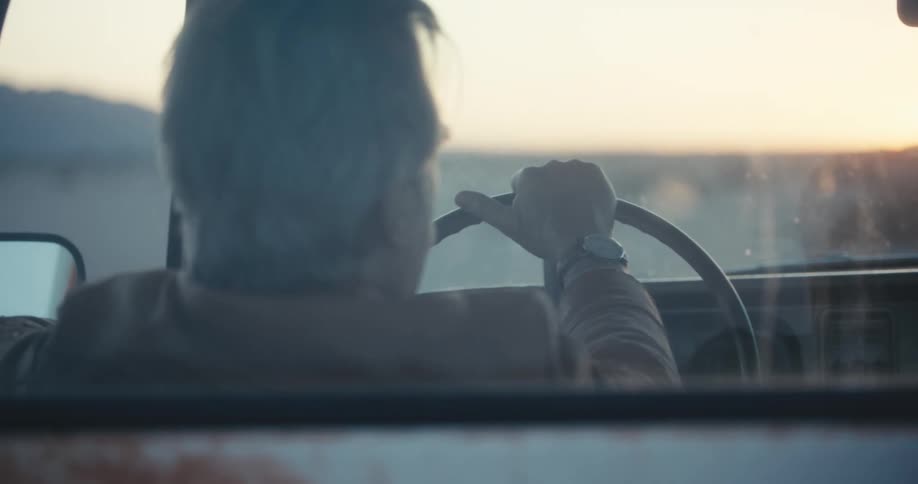 An elderly man is driving a car at dusk