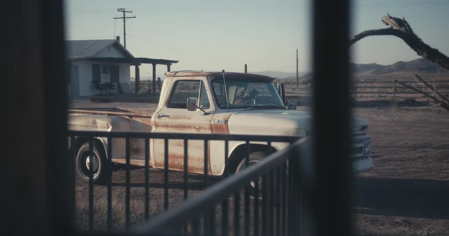 Man gets out of beat up vintage truck in front of house on desert ranch