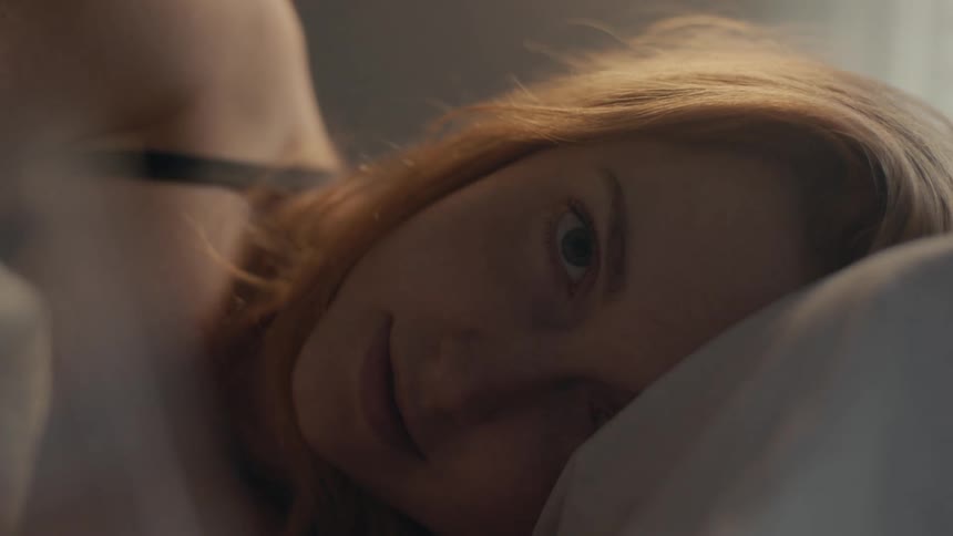 A woman laying on her side in bed opens her eyes and smiles warmly
