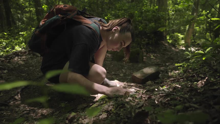 Young female with backpack explores the ground in the forest
