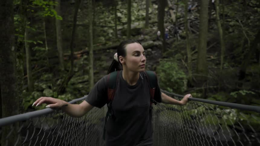 A woman hikes across a wire fenced bridge in a forest area