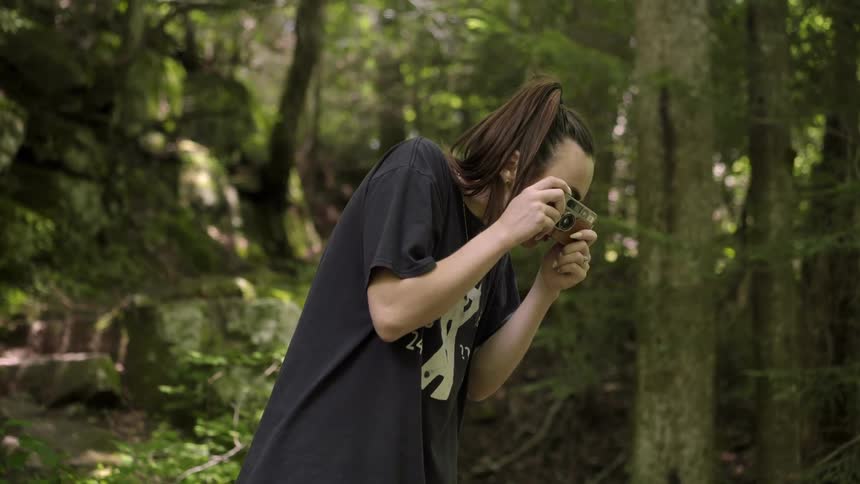 Young woman takes pictures with a small camera in the forest