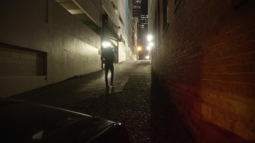 Man walking away from a car parked on an alleyway in the city at night
