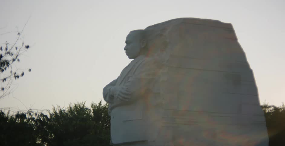 A statue of martin luther king jr with trees the sky and clouds in the background