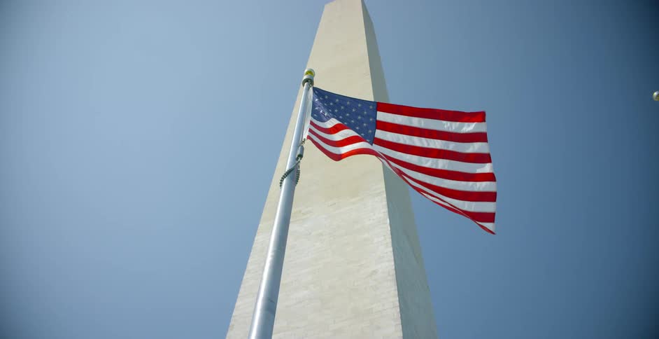 American flag flaps in breeze near washington monument under blue sky