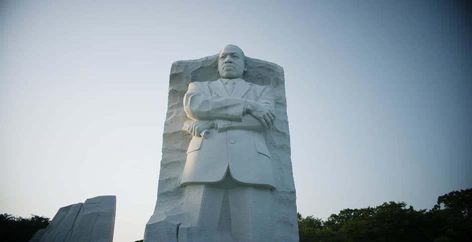 White monument of standing man contrasts with tree tops under clear sky