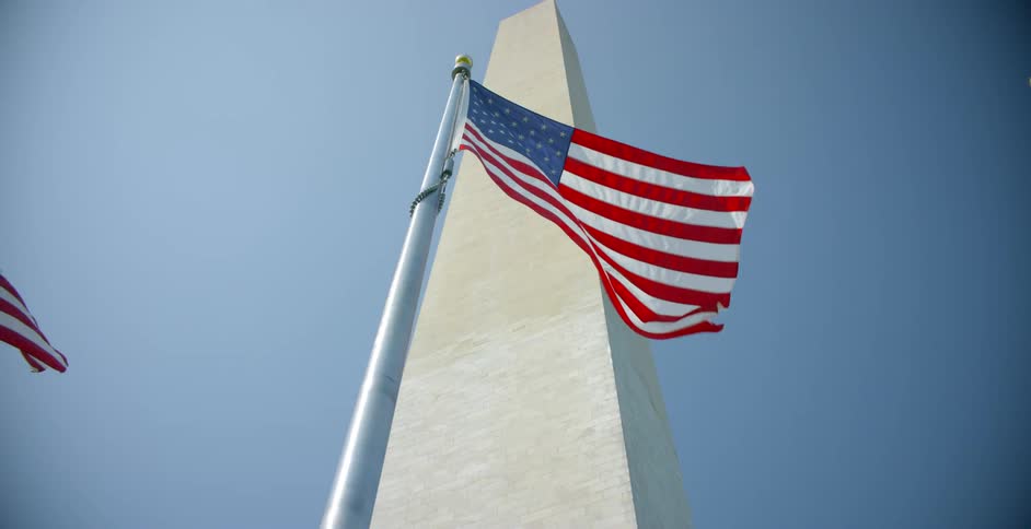 American flags flutter in the wind near monument under clear blue sky