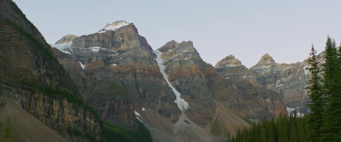 A snow sprinkled mountain ridge of gray and brown stone under a clear daytime sky